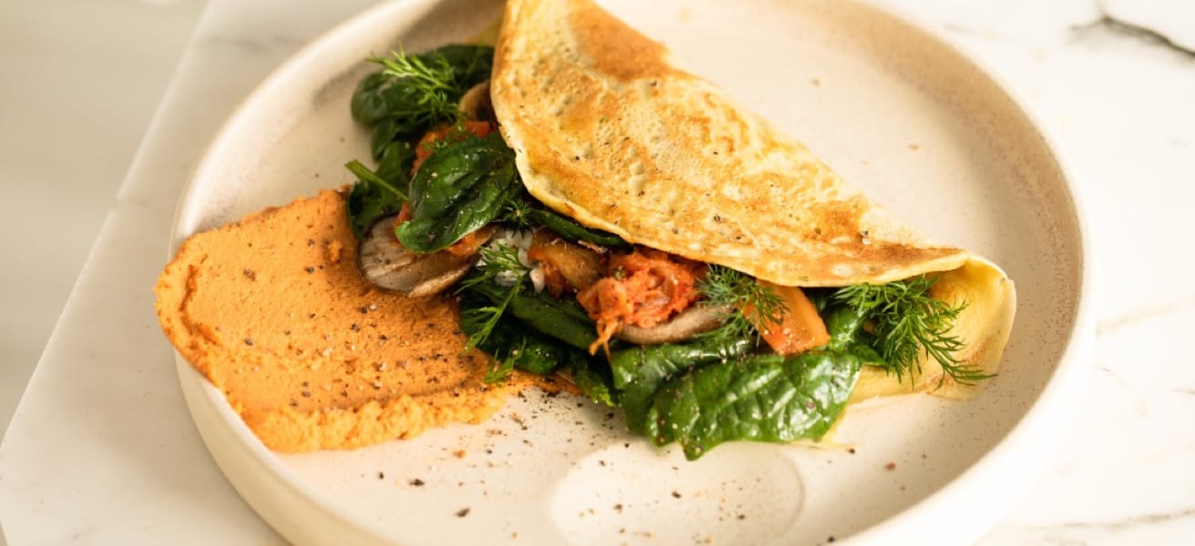 A plated omelette folded over sautéed greens, mushrooms and peppers, garnished with fresh dill.